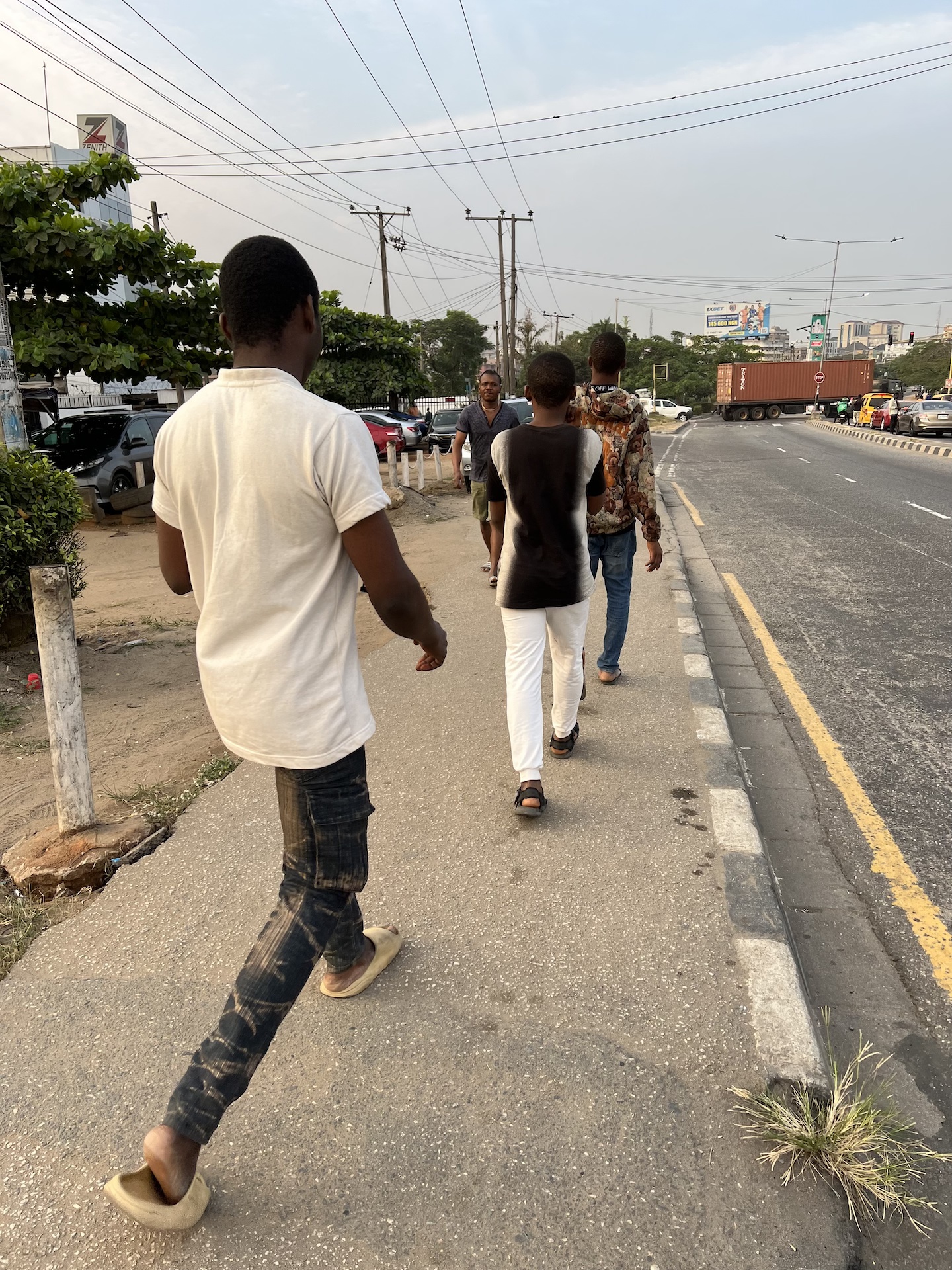 Newman, Chinecherem, and Bobo walking in single file after alighting from the Keke Napep, on our way to the next bus stop in hopes of catching a vehicle.