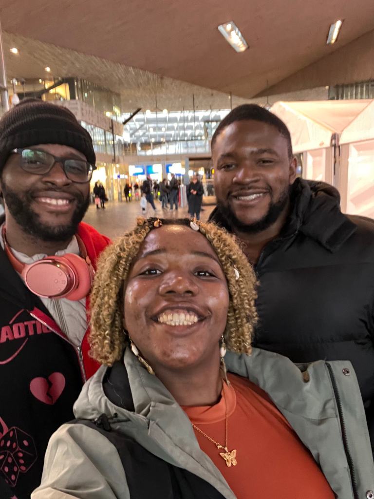 Shalvah, Timmy, and I sharing a smile, gathered for a selfie with a bustling station background